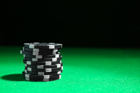 Stack of poker chips on green table against dark background, closeup. Space for textの写真素材