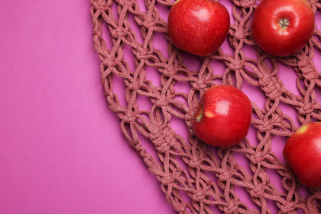 Handmade macrame shopping bag with apples on crimson background, top view