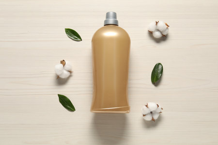 Bottle with laundry detergent, cotton flowers and green leaves on wooden background, flat layの写真素材
