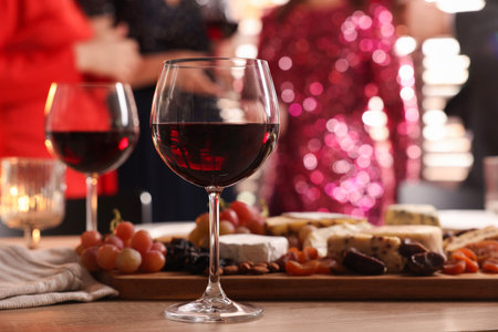 People holding glasses of wine at party, focus on wooden table with snacks and alcoholの写真素材