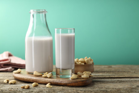 Fresh cashew milk in glass, bottle and nuts on wooden table against green background, closeup. Space for textの写真素材