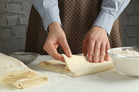 Woman making puff pastry dough at white table, closeup