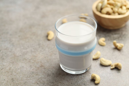 Fresh cashew milk in glass and nuts on gray textured table, closeup. Space for textの写真素材