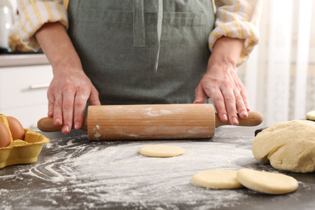 Making pirozhki (stuffed pastry pies). Woman shaping dough with rolling pin at gray table, closeup