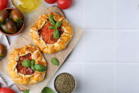 Tasty galettes with tomato and basil on white tiled table, flat lay. Space for textの写真素材