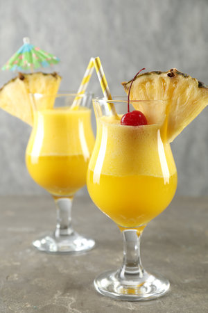 Tasty pineapple cocktail in glasses served on gray table