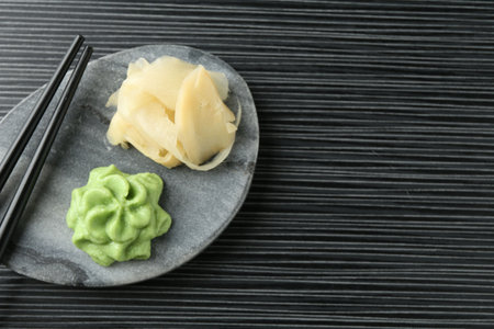 Hot wasabi paste, ginger and chopsticks on black textured table, top view. Space for textの写真素材