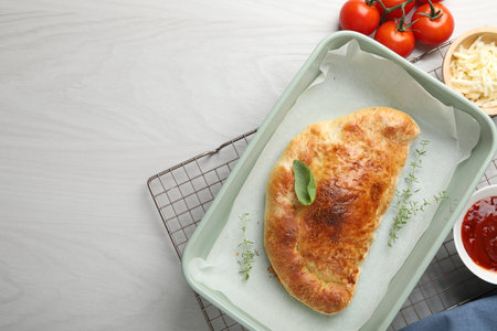 Delicious calzone pizza in baking dish and ingredients on white wooden table, flat lay. Space for textの写真素材