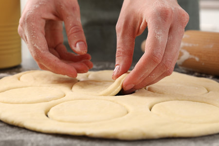 Woman making pirozhki (stuffed pastry pies) at gray table indoors, closeup