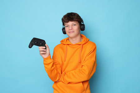 Person in orange hoodie with gaming controller against light blue backgroundの写真素材
