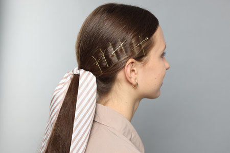 Person with hair clips and striped bandana on light grey background, back view