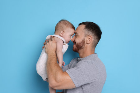 Father with his cute baby on light blue background