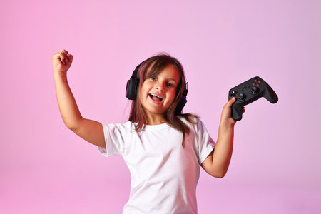 Happy little girl in headphones with controller on pink backgroundの写真素材