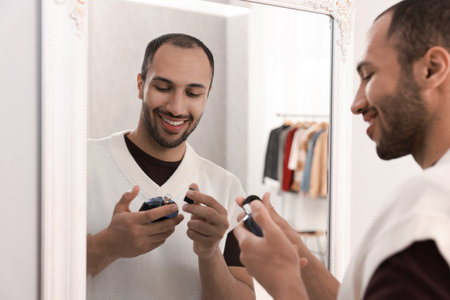 Smiling man spraying perfume near mirror at homeの写真素材