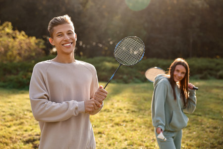Young man and woman with badminton rackets and shuttlecock in park on sunny day, selective focusの写真素材
