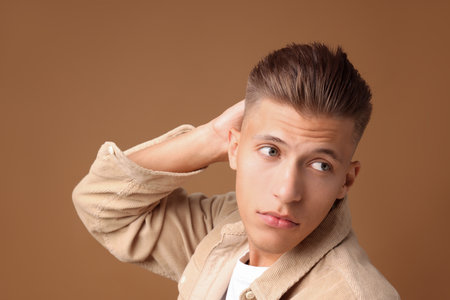 Confident young man with stylish haircut on brown backgroundの写真素材