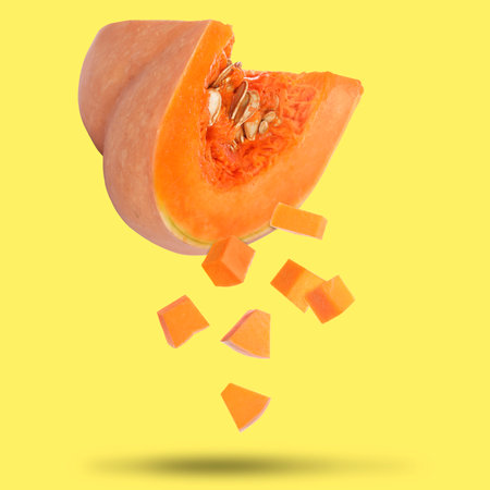 Pieces of fresh raw pumpkin falling on yellow backgroundの写真素材