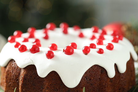 Traditional Christmas cake decorated with red currants against blurred background, closeup