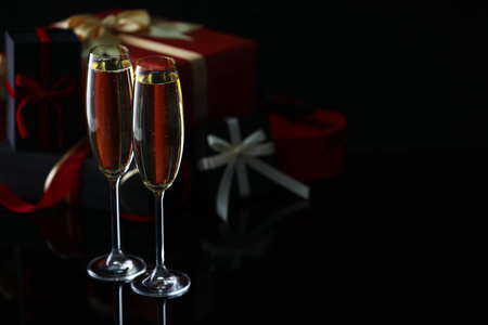 Delicious champagne in glasses and Christmas presents on black mirror surface, closeup. Space for textの写真素材