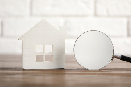 House hunting. Magnifying glass and house figure on wooden tableの写真素材