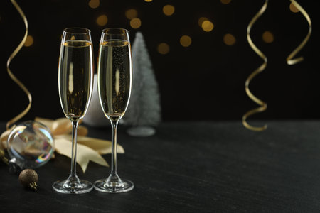 Delicious champagne in glasses and Christmas decor on black table against blurred lights, space for textの写真素材
