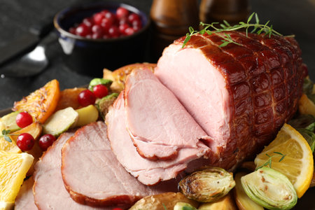 Tasty baked ham served with vegetables and oranges on black table, closeupの写真素材