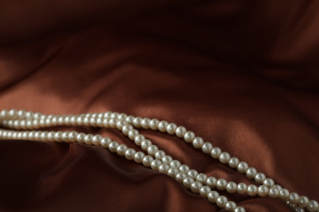 Beautiful pearl necklace on brown silk, closeup