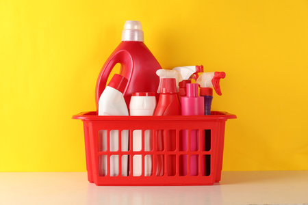 Different cleaning products in basket on table against yellow backgroundの写真素材