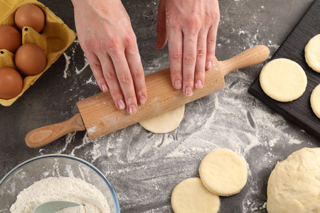 Making pirozhki (stuffed pastry pies). Woman shaping dough with rolling pin at gray table, top view