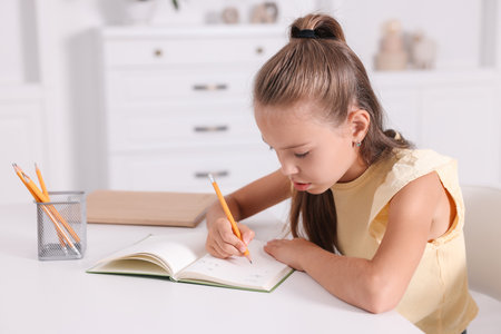 Girl with incorrect posture doing homework at white desk indoorsの写真素材