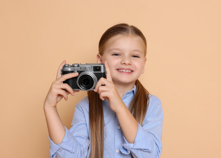 Little girl with camera pretending to be photographer on beige background. Dreaming of future professionの写真素材