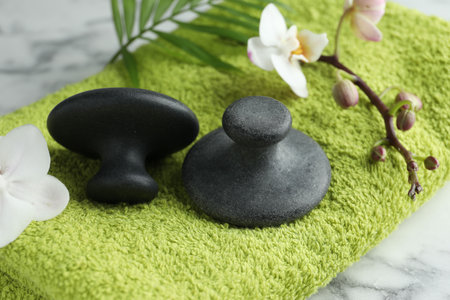 Spa stones, orchid branch, palm leaf and towel on white marble table, closeup