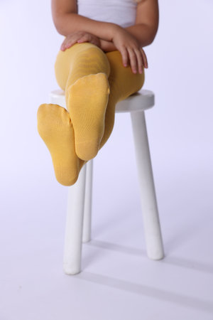 Child in bright tights sitting on stool against white background, closeupの写真素材