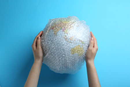 Woman holding globe packed in bubble wrap on turquoise background, top view. Environmental...