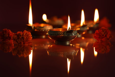 Diwali celebration. Diya lamps and beautiful flowers on dark background, closeup