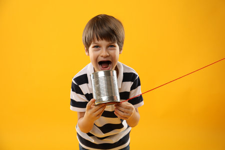 Boy using tin can telephone on yellow backgroundの写真素材