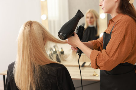 Hairdresser blow drying client's hair in salon, closeupの写真素材