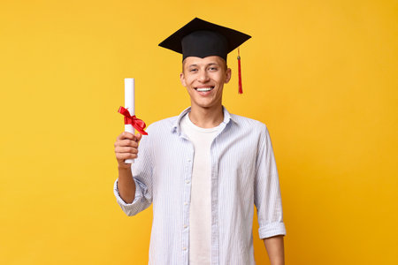 Happy student with diploma after graduation on orange backgroundの写真素材