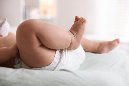 Cute little baby in diaper on bed indoors, closeup