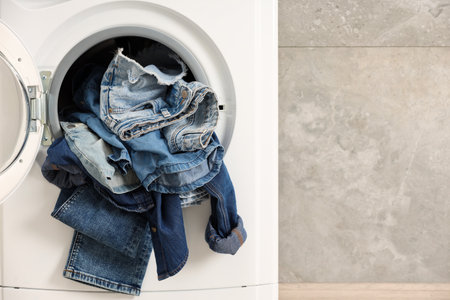 Washing machine with dirty jeans and other denim clothes indoors, space for textの写真素材