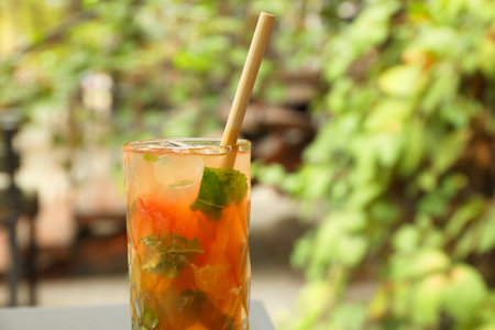 Glass of tasty refreshing drink and straw outdoors, closeup