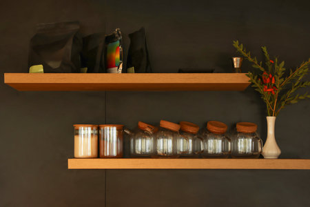Jars with sugar, bags of coffee and decor on wooden shelves on dark wallの写真素材