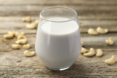 Fresh cashew milk in glass and nuts on wooden table, closeupの写真素材