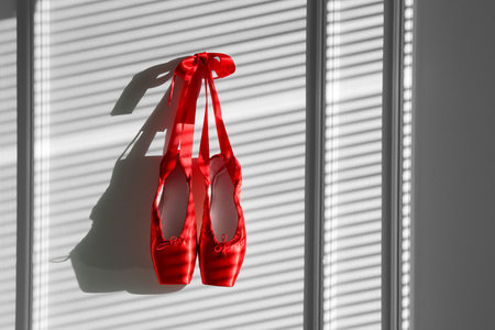 Pair of beautiful red pointe shoes hanging on white wall, space for textの写真素材