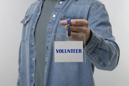 Man holding badge with the word Volunteer on gray background, closeup