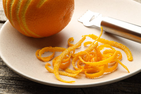 Fresh orange zest, fruit and zester on wooden table, closeupの写真素材