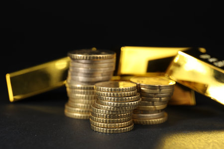 Gold bars and coins on black table, closeup