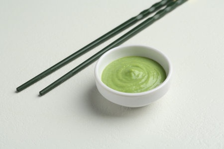 Hot wasabi paste in bowl and chopsticks on light textured table, closeupの写真素材