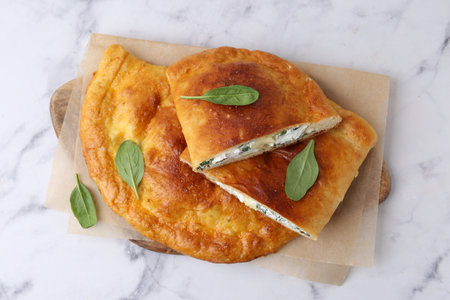 Tasty calzones with cheese and basil on white marble table, top view