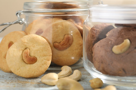 Different tasty cashew cookies in jars on light wooden table, closeup